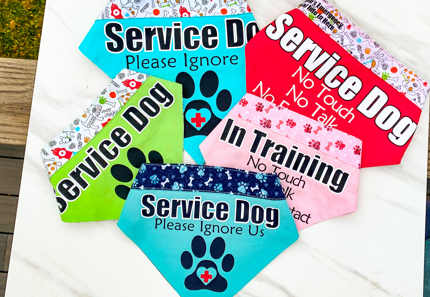 5 service dogs bandana on a marble slab. The bandanas are in the colors aqua, green, red, pink, and blue.