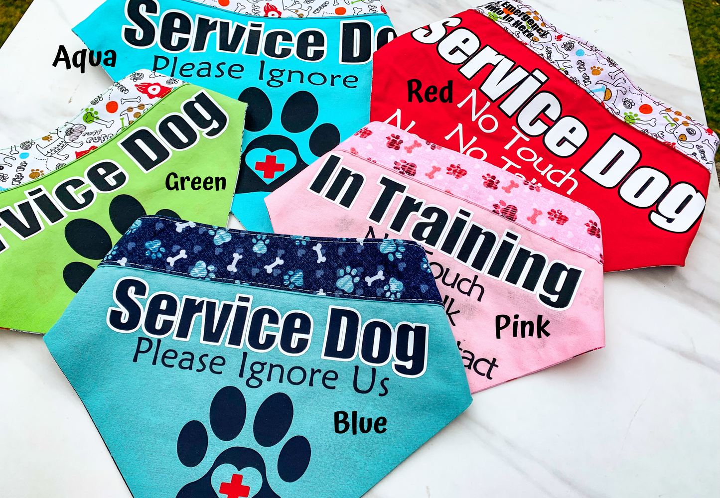 5 Bandanas are shown on a white marble background. The bandanas are labeled with their colors- Aqua, Green, Red, Pink, and Blue.