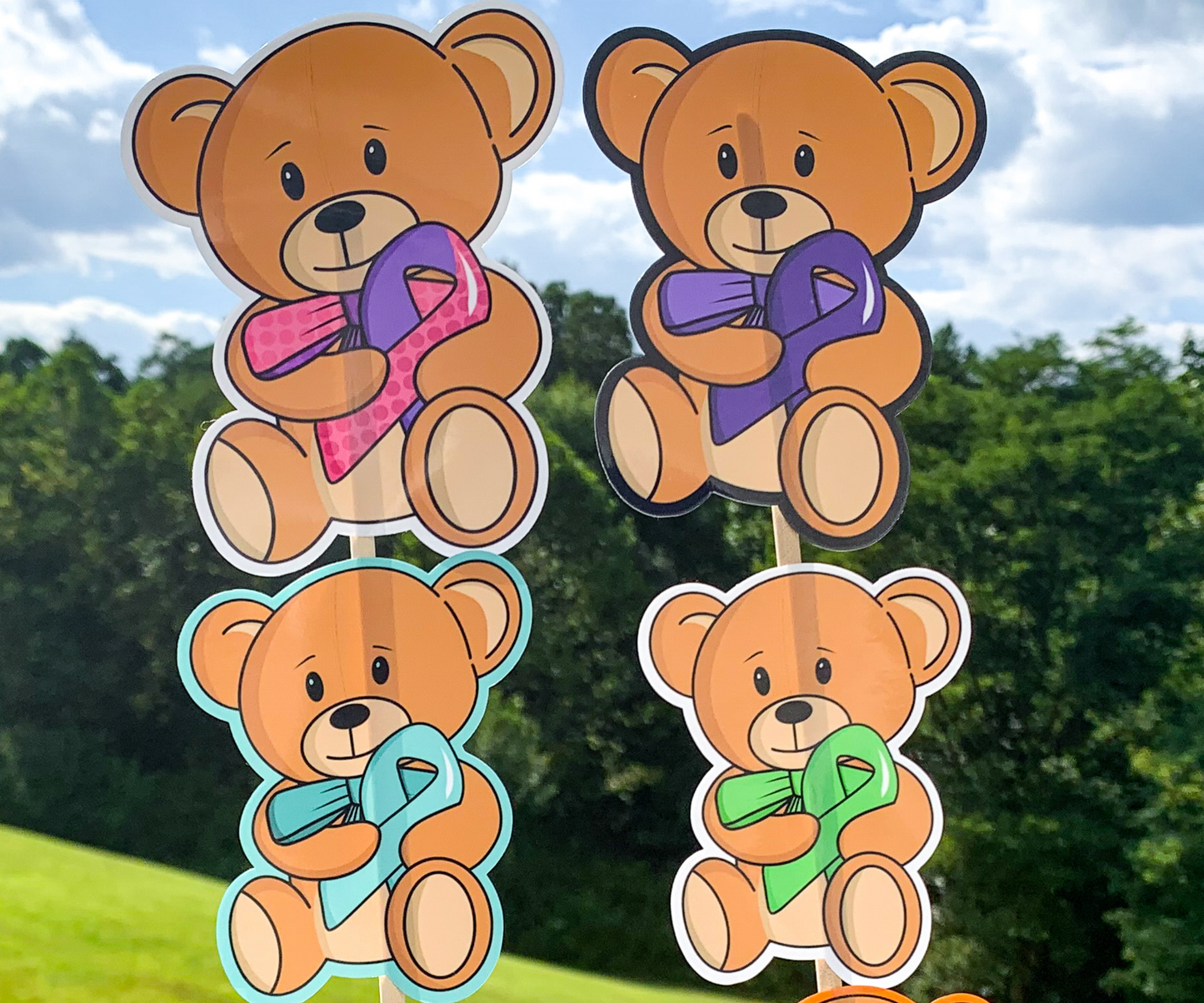 4 stickers are shown on sticks. The stickers are brown teddy bears holding an awareness ribbon with a matching colored bow tie. They are very cute. 2 stickers have white borders, 1 has a black border to blend in with the outline of the bears, and 1 sticker has a bright turquoise colored outline that is the same color of the awareness ribbon.