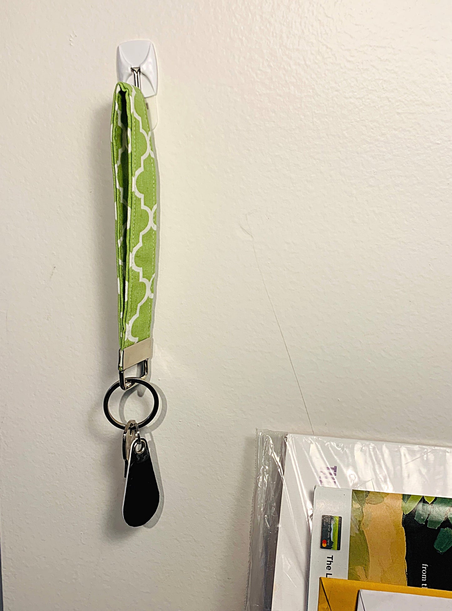 A green keychain is shown hanging on a small command hook on the wall. There is a key and black fob attached to the key ring.