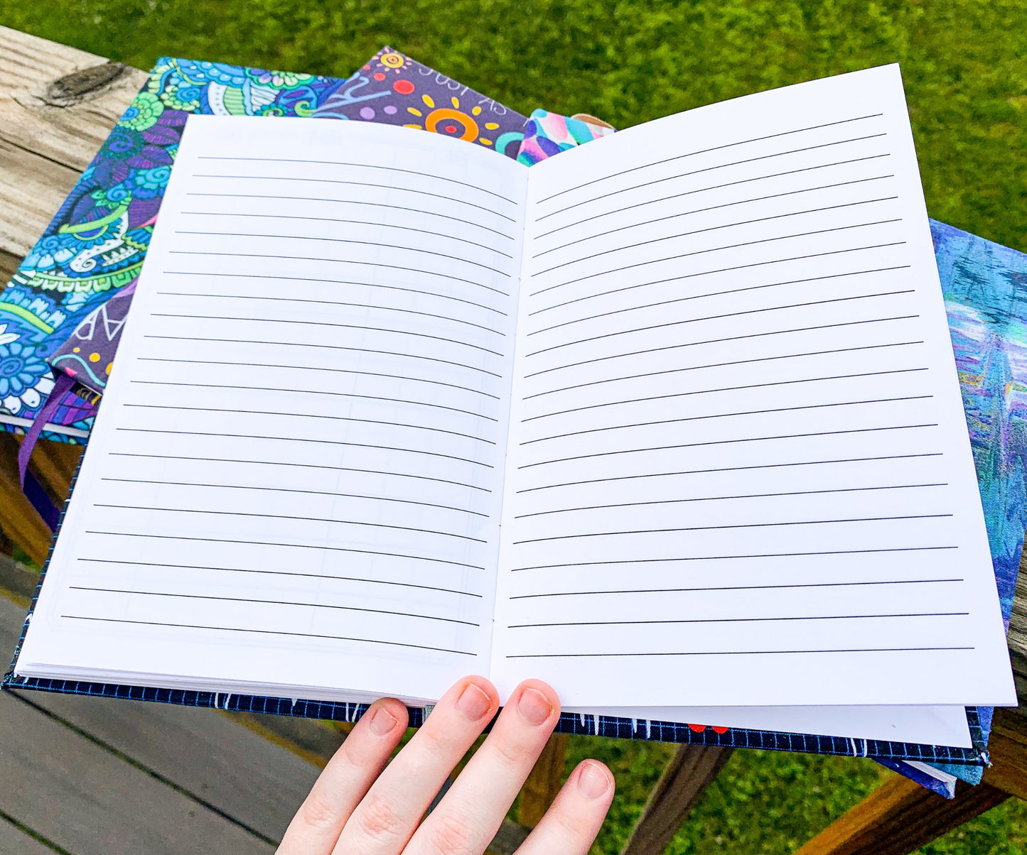 A book is open to lined pages, this is the back of the book. The book is sitting on top of multiple books with patterned covers.