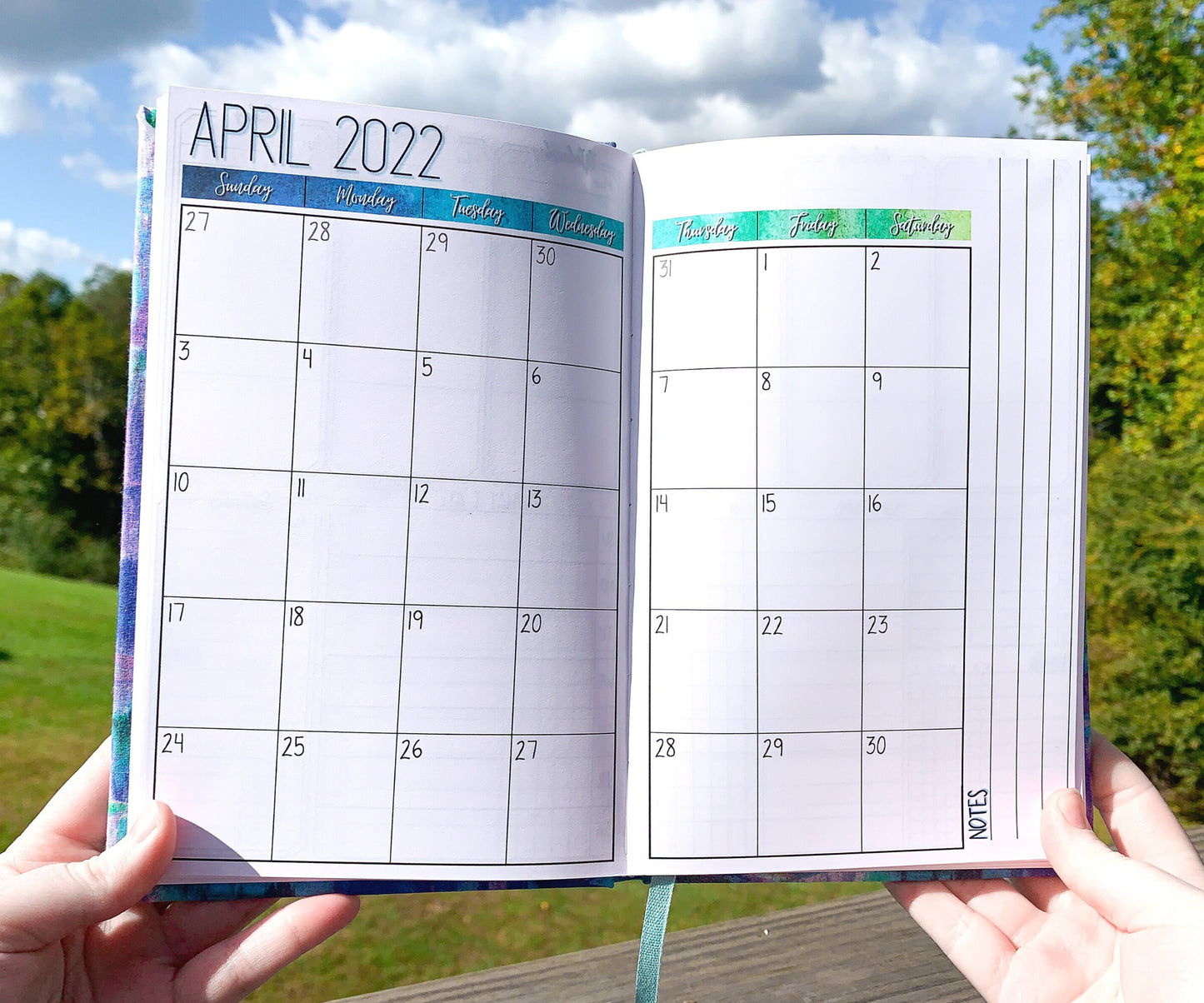 The monthly page is shown. This a calendar page with the month name and year at the top right and a notes writing area on the right side of the calendar box. There is a blue gradient from dark blue to aqua to green where the days of the week are- this is for the blue color journal.
