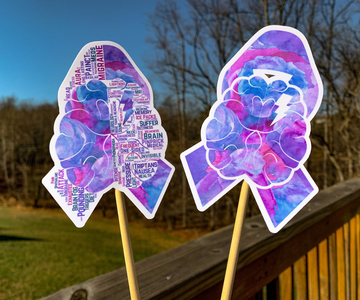 The word cloud and watercolor designs are shown on 2 sticks. Both ribbons feature purple borders with a magenta center color awareness ribbon with a brain in the center that has a lightning bolt on just the upper right side. The word cloud design on the left is split in half with a word cloud on the left half of the ribbon and right half of the brain.