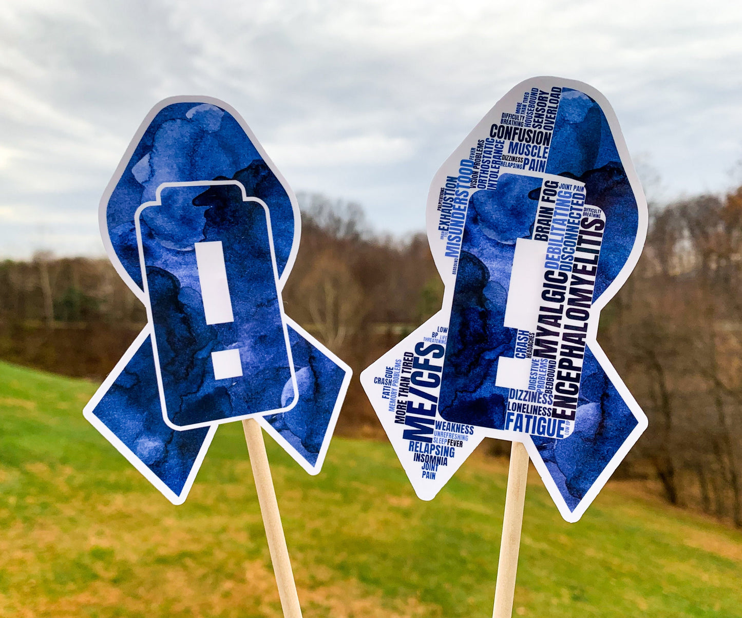 The word cloud and watercolor designs are shown on 2 sticks. Both ribbons feature a dark blue color awareness ribbon with a critically low battery, battery with an exclamation point, in the center. The word cloud design on the left is split in half with a word cloud on the left half of the ribbon and right half of the battery.