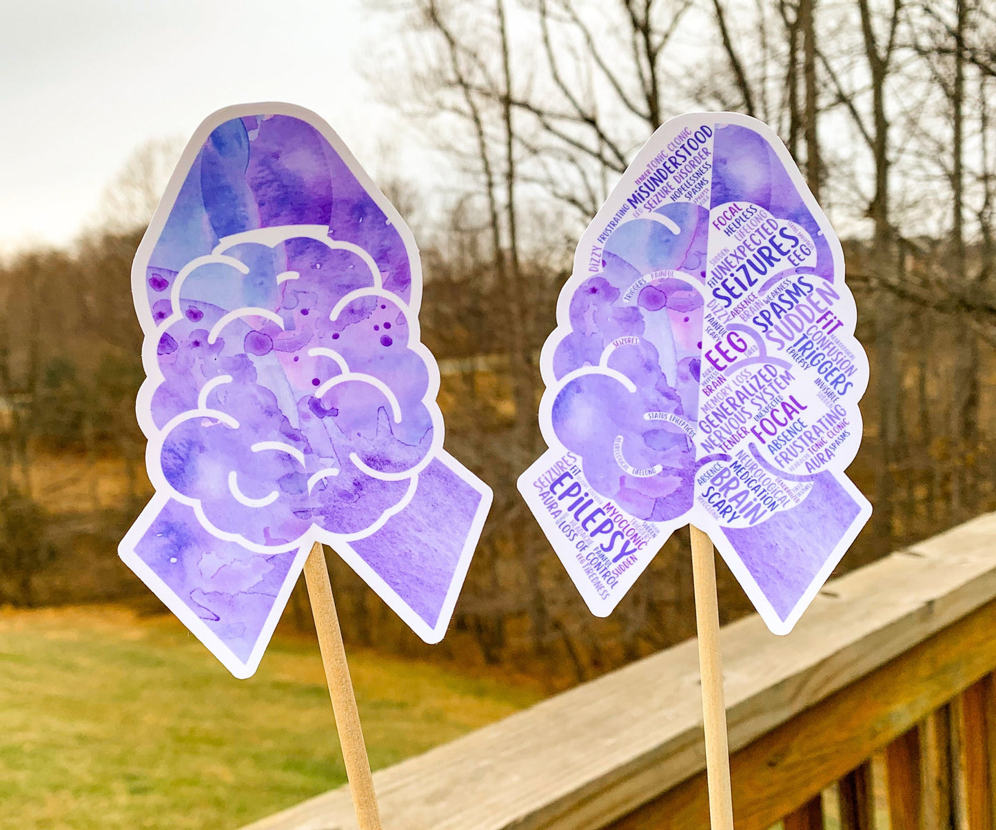 The word cloud and watercolor designs are shown on 2 sticks. Both ribbons feature a purple color awareness ribbon with a brain in the center. The word cloud design on the left is split in half with a word cloud on the left half of the ribbon and right half of the brain.