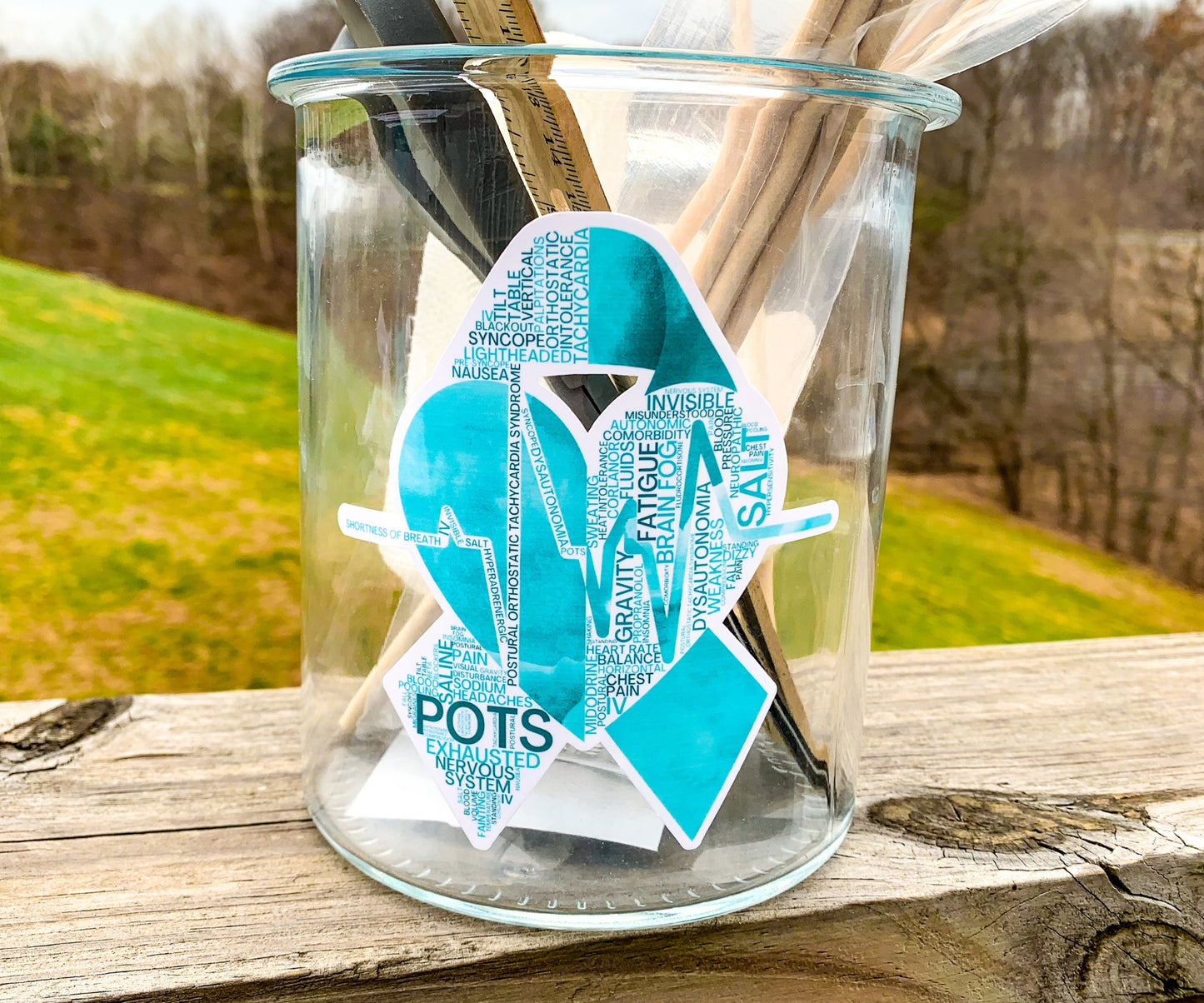 A tall 4.5 inch Teal POTS word cloud sticker is shown on a glass jar. This is for an example of surfaces it can stick to.