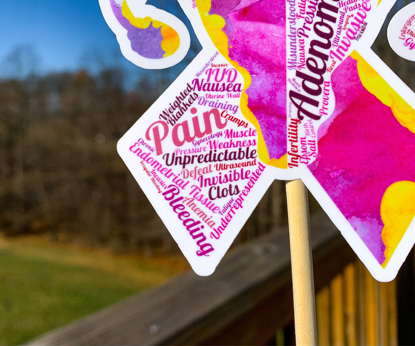 A close up is shown of the word cloud ribbon. You can see the words clearly in matching magenta and pink colors. The words are things like Pain, Cramps, Uterine Wall, IUD, Bleeding, Endometrial Tissue, Clots, Pressure, Unpredictable, and more.
