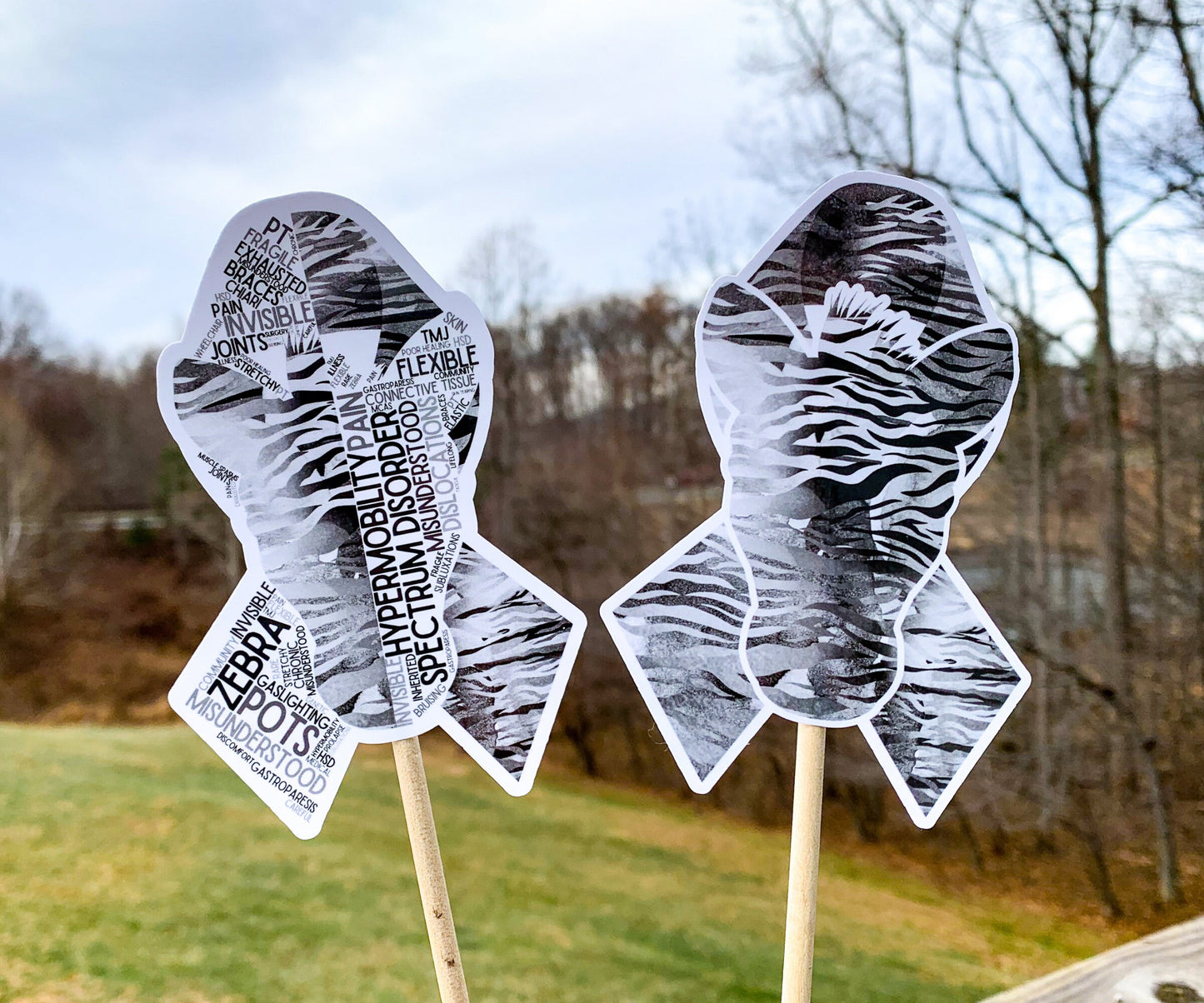 The word cloud and watercolor designs are shown on 2 sticks. Both ribbons are black and grey zebra stripes with a zebra head in the center. The word cloud design on the left is split in half with a word cloud on the left half of the ribbon and right half of the zebra. The right watercolor ribbon is all zebra patterened with a white border around the zebra for definition.