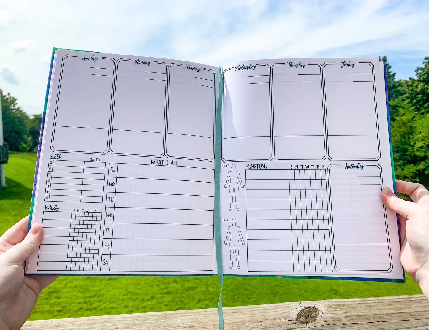 The large print symptom journal is shown open. It has 6 boxes at the top and 1 below on the right, each is a day of the week. The boxes take up half the page vertically they have a line towards the bottom. Bottom left are sleep, meds, and a what I ate sections divided into writing slots for each day. The med box has space 7 meds and 2 checkboxes per day. The symptom box on the right side has 10 slots. There are 2 body outlines, front and back, to the left of the symptom box.