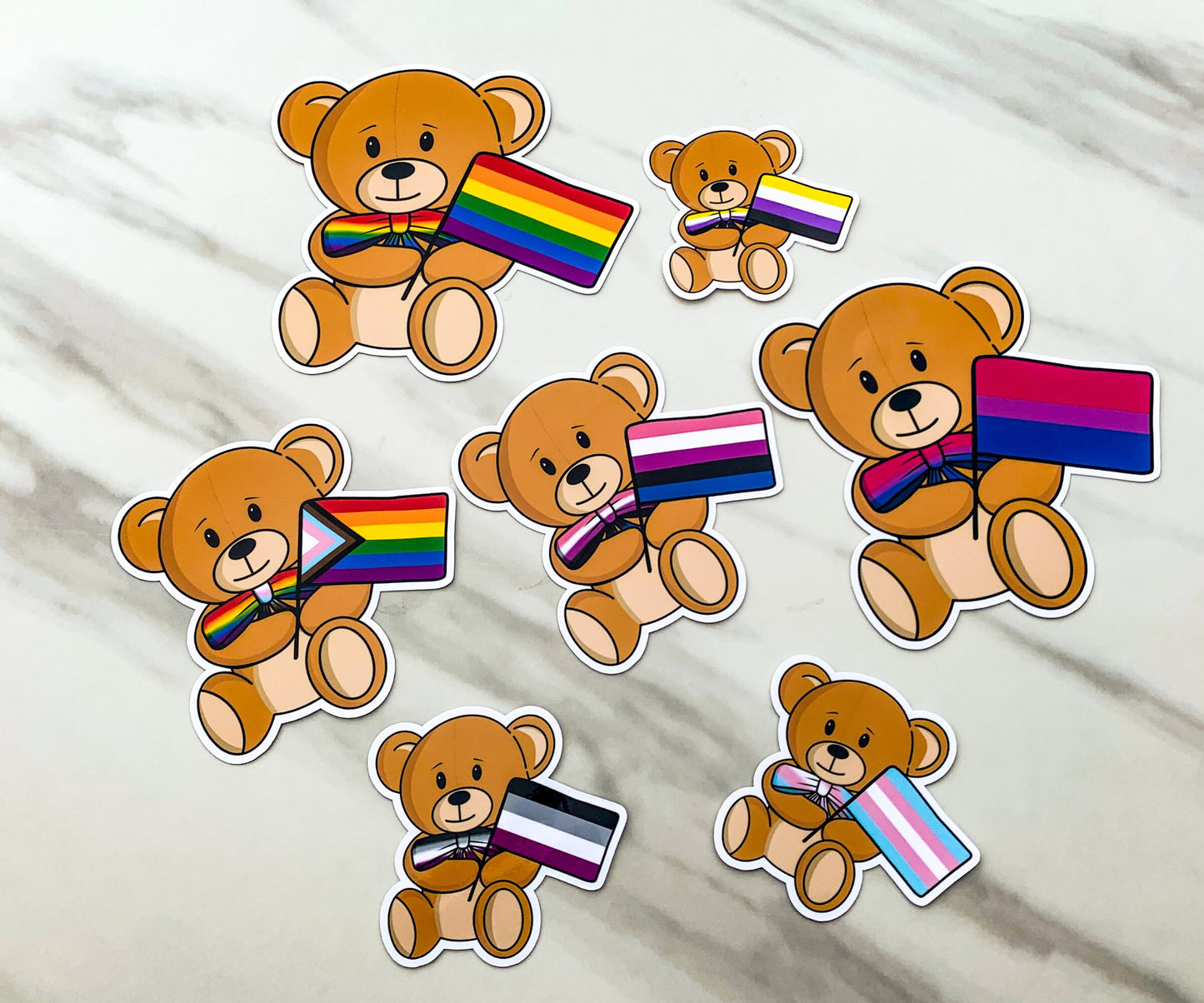 7 pride flag bears are shown on a marble surface. They each have different pride flags that match their bow ties.