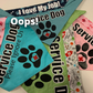 4 Bandanas are shown. One in Aqua and Pink, one in Blue and navy, another in green and white pattern, and the last at the bottom in pink. All say service dog on them with a paw, one says Please Ignore Us in addition. White letters say Oops!