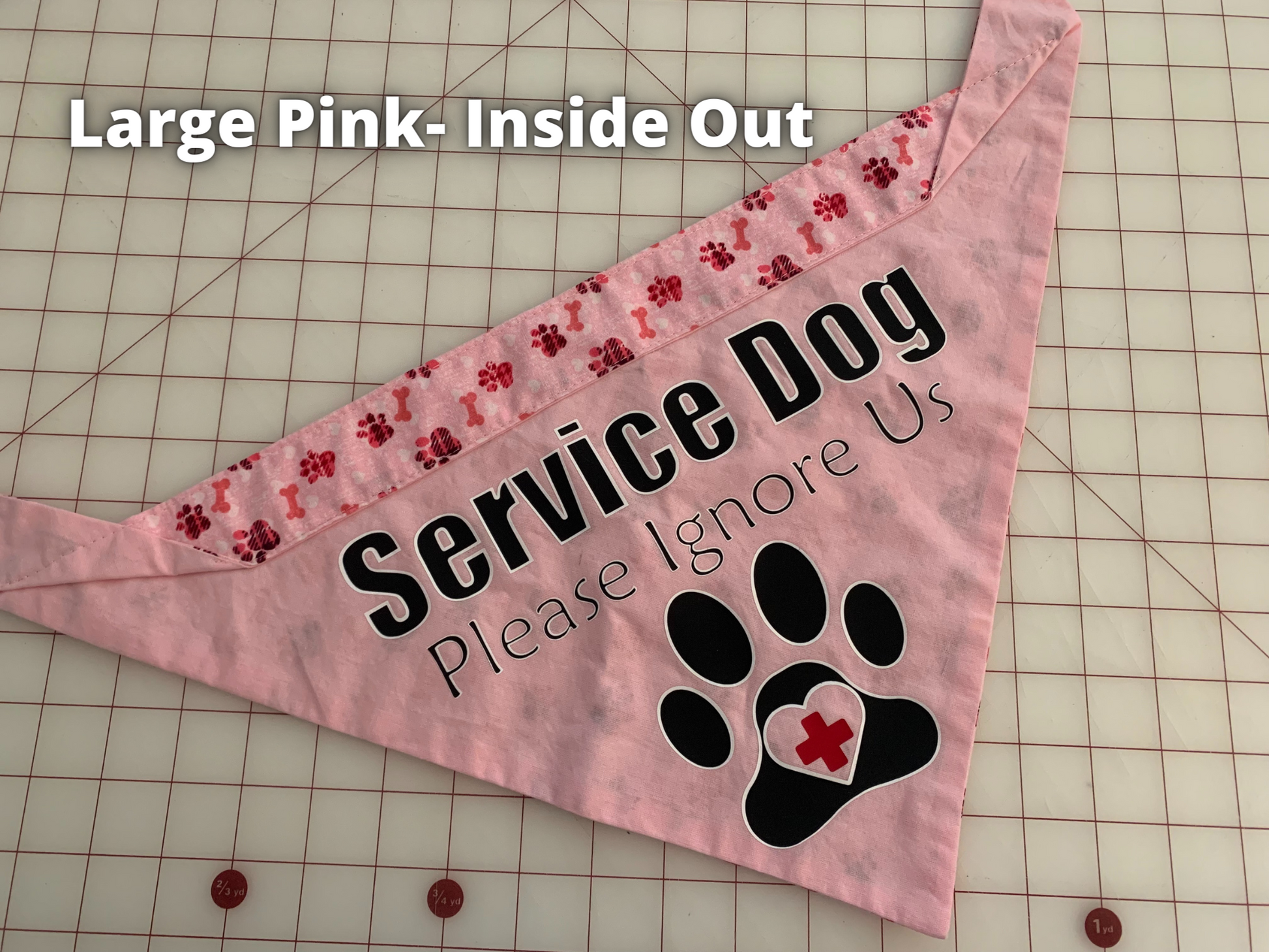A pink bandana is shown on a white grid surface. Text says Large Pink Inside Out. The Bandana is all pink with a pink paws and bones contrast. The black text is the same as the previous bandana but is narrower. Please Ignore Us and Paw also have a white outline.