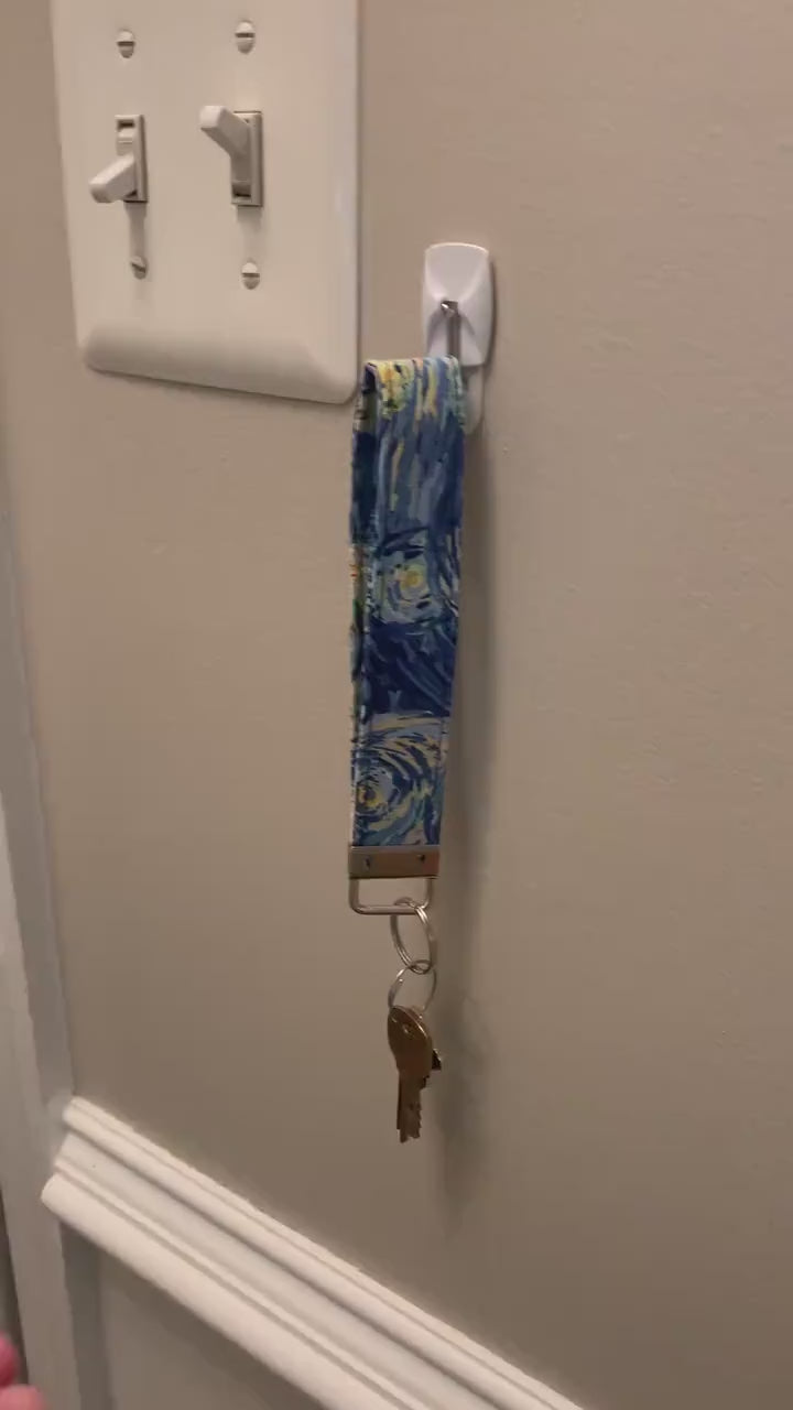  A video showing a starry night colored wristlet with keys attached is shown being taken off a hook on the wall and slipped on handed onto a wrist