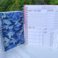 2 spiral bound books are standing up on a marble surface. The smaller one is closed and has a blue and gold floral cover. The other is open showing the interior pages. It has alternating light and dark pink tabs that are blank. The page has several sections and the titles have a pink shadow.
