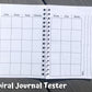 The spiral journal tester is shown open to the calendar page. There are 7 columns, 5 rows deep of squares with no dates. At the top of each column are the days of the week, but no color background. On the right page next to the box of squares you there are 3 vertical lines lining perpendicular to the way info would be written in the boxes. Notes is written on the left of the top line when facing to write. 