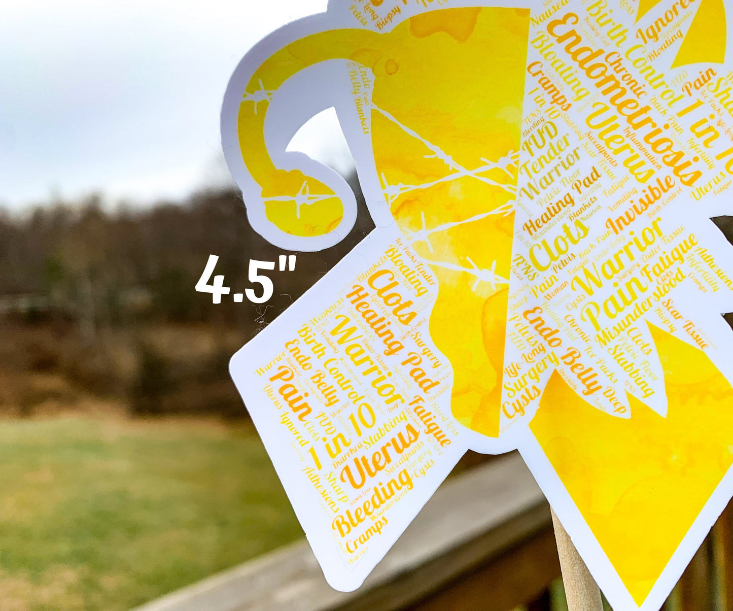 A close up of the 4.5 in word cloud ribbon is shown. You can see the words clearly in matching yellow and orange colors. The words are things like Heating Pad, Clots, Bloating, Birth Control, Endo Belly, 1 in 10, Bleeding, Tender, IUD, Chronic, Warrior, Deep, Cysts, and more.