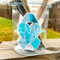 A tall 4.5 inch Teal POTS word cloud sticker is shown on a glass jar. This is for an example of surfaces it can stick to.