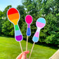 3 more Pride Spoon stickers are shown on sticks. The 6.5 inch rainbow spoon has the normal 6 rainbow colors horizontally. The 4.5 inch bisexual pride spoon has magenta, purple, and royal blue stripes horizontally with the purple being smaller. The 5.5 inch transgender spoon has the same colors and horizontal lines as the one in the previous photo, but is larger.