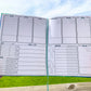 The large print symptom journal is shown open. It has 6 boxes at the top and 1 below on the right, each is a day of the week. The boxes take up half the page vertically they have a line towards the bottom. Bottom left are sleep, meds, and a what I ate sections divided into writing slots for each day.  The med box has space 7 meds and 2 checkboxes per day. The symptom box on the right side has 10 slots. There are 2 body outlines, front and back, to the left of the symptom box.