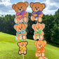 The same bears shown before are shown again on sticks. The purple and yellow bears have black outline, the turquoise and orange bears have matching outlines, and the purple pink dot and green bears have white outlines.