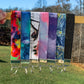  6 wristlets are shown hanging on a wood stick. The wristlets are 1 inche wide fabric folded over with a silver colored metal bracket at the bottom with a split key ring on it. The wristlets are in the colors Brushstrokes rainbow, glamour, pink clouds, brushstrokes purple, starry night,, and 2 unlisted.