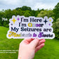 A 7 inch sticker is shown being held up. The sticker says I'm Here I'm Queer My Seizures are Moderate to Severe. Queer and Moderate to severe are in non binary flag colors with corresponding sparkles next to I'm Here I'm Queer. A note says sizes are approximate, may vary based on text requested.