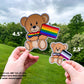 A 4 1/2 inch and 2 1/2 inch sticker are shown held up next to each other for comparison. The 4 1/2 inch sticker has a rainbow pride flag, the bow tie is a matching rainbow gradient. The 2 1/2 inch sticker has a asexual flag with a matching gradient bow tie. A note says all stickers are .666 inch not 1/2 inch but the number have been rounded for easier measurement.
